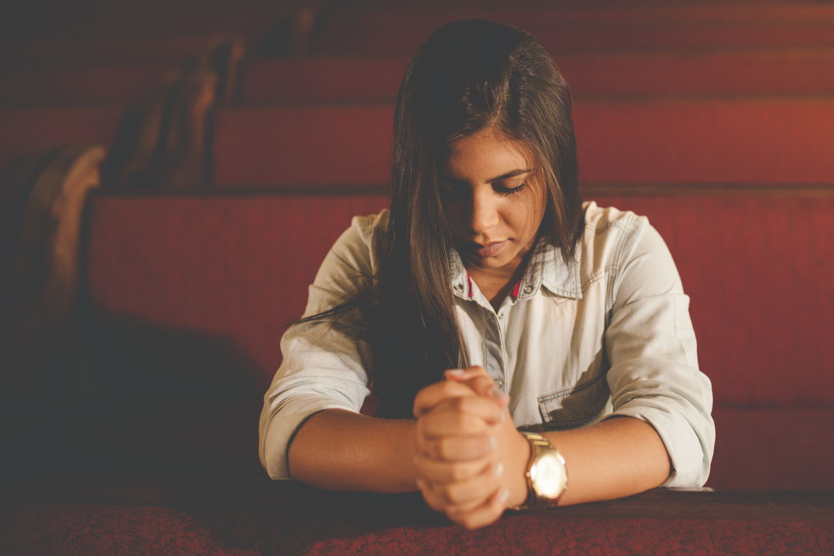 Mulher orando em igreja, representando o versículo Orai sem cessar