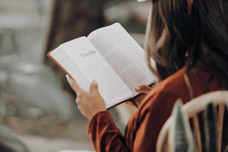 Mulher de costas lendo a bíblia no livro de Provérbios. 