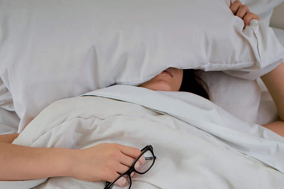 Mulher deitada na cama, com o travasseiro sobre o rosto representando os Versículos sobre preguiça - Imagem apenas decorativa