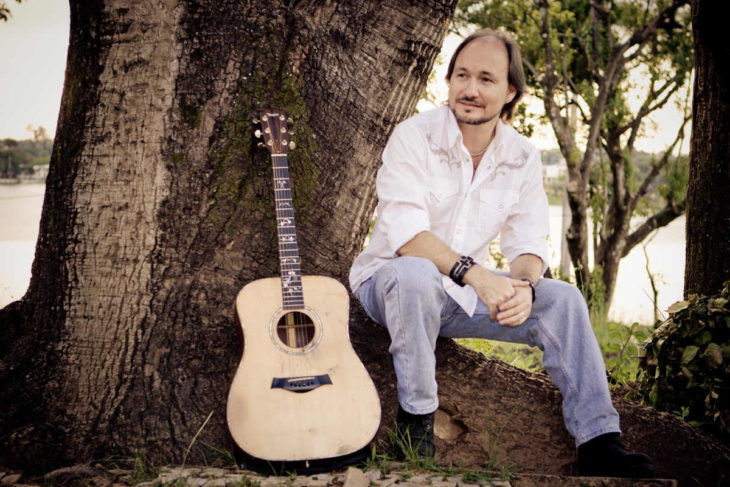 David Quinlan sentado na árvore com seu violão ao lado